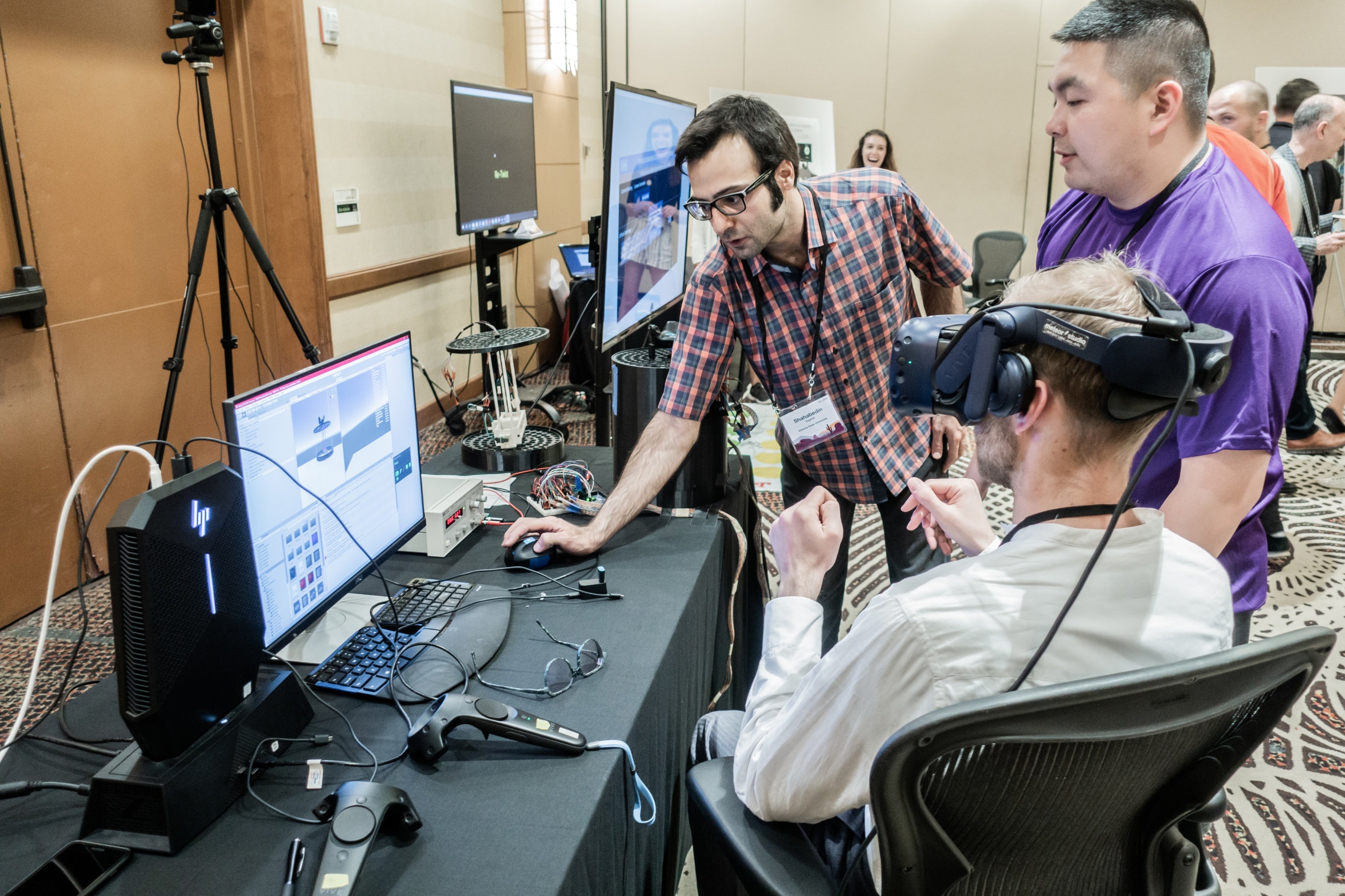 man sitting in chair with VR headset on, while an ASU staff member sets up the program on the computer